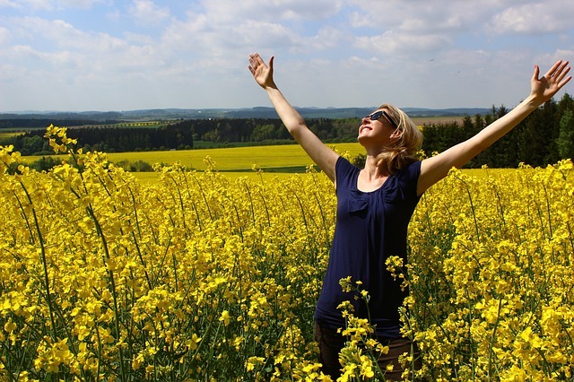 Photo of a woman in a field with arms outstretched.