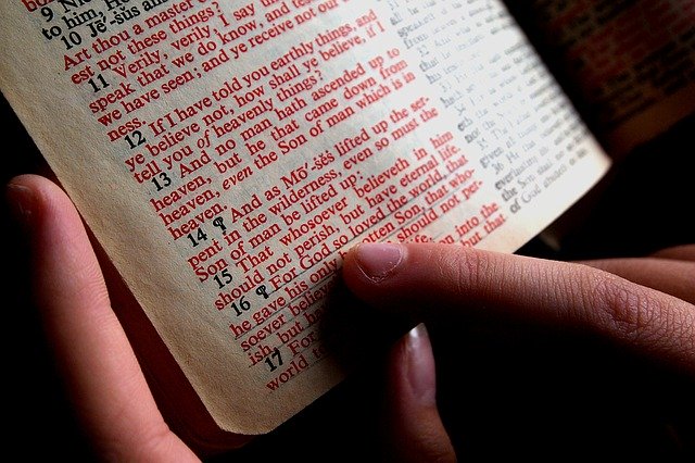 Photo of a Bible opened to John 3:16, with a finger hovered over the underlined red words.